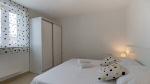 A bedroom with a bed, pillows, a wardrobe, and a window with polka dot curtains.