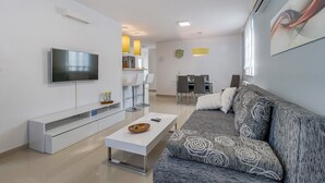 A modern living room with a flat-screen TV, a sofa, a coffee table, and a dining area with chairs and a table.