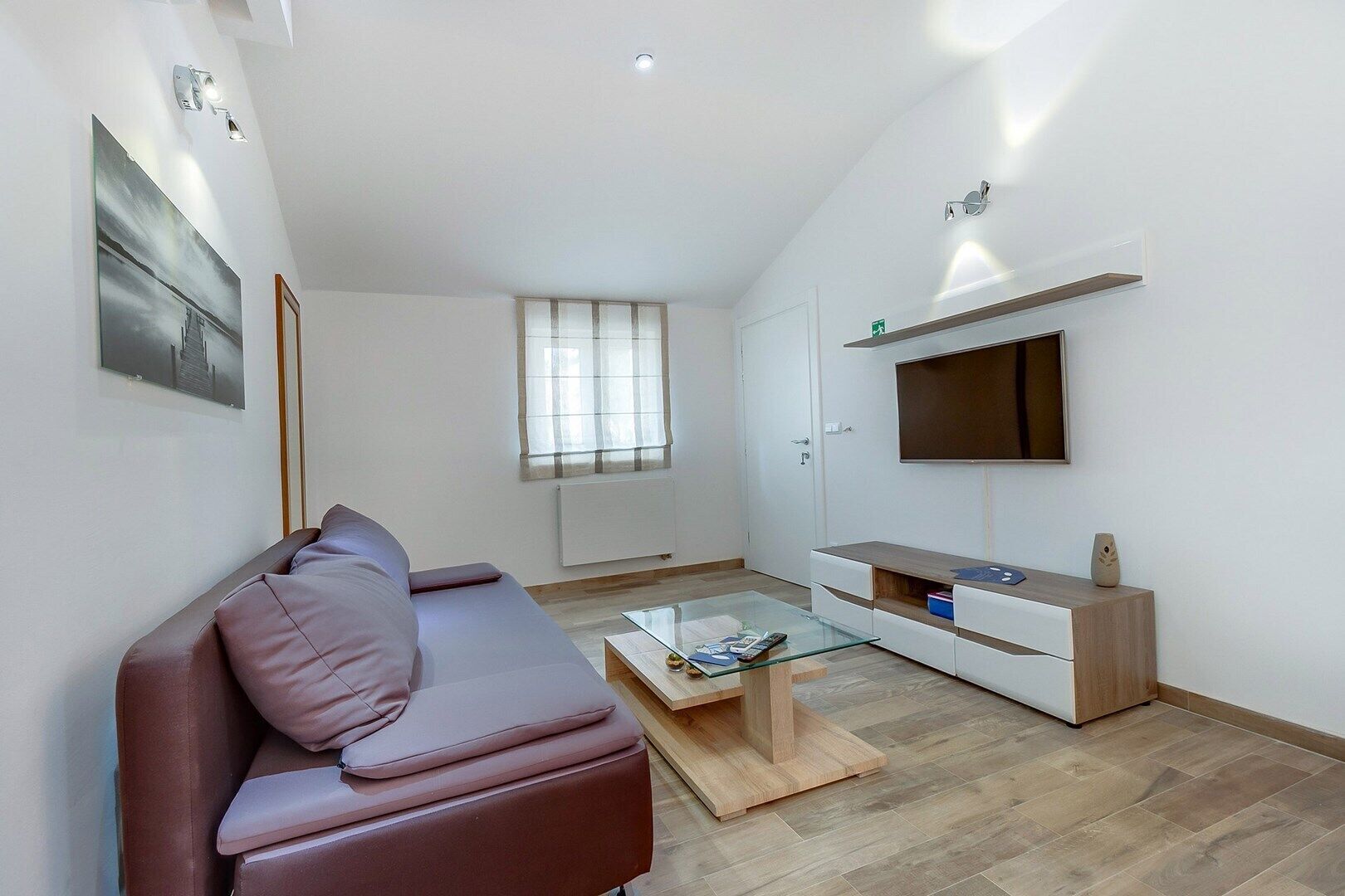 Una sala moderna con un sofá de cuero marrón, una mesa de centro de vidrio y un televisor sobre un mueble de madera.