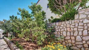 Un mur de pierre bordé d’un jardin, avec des arbres et des fleurs jaunes.