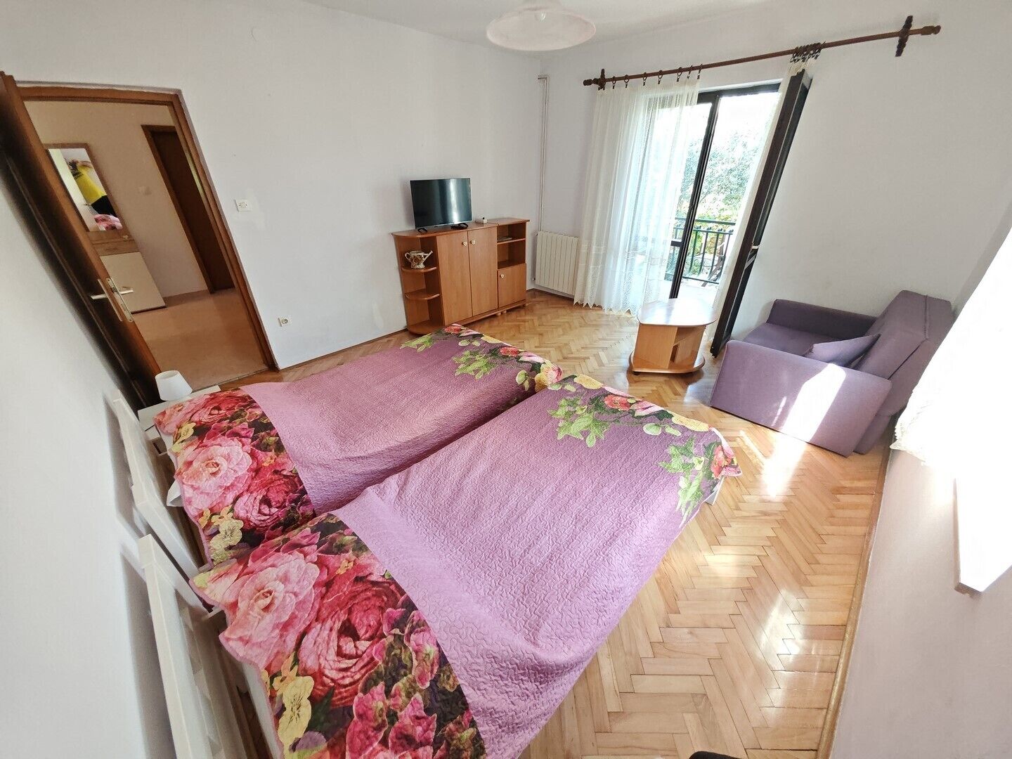 A bedroom with a bed, a TV, a wardrobe, and a balcony with curtains.