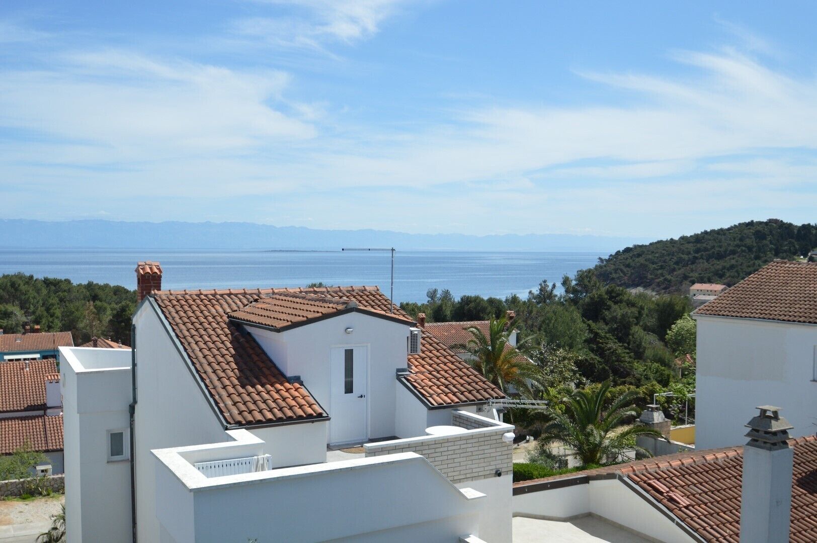Ein Küstenwohngebiet mit Terrakotta-Dachziegeln, weißen Gebäuden und Blick auf das Meer.