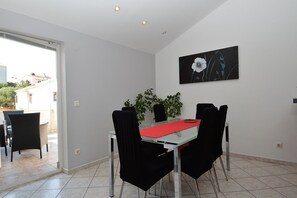 Un coin repas avec une table en verre, des chaises noires, un chemin de table rouge et une plante en pot.