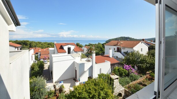 A residential area with white buildings and red-tiled roofs, surrounded by greenery and a clear blue sky.