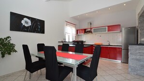 A modern kitchen with red cabinets, a stainless steel refrigerator, and a dining area with a glass table and black chairs.