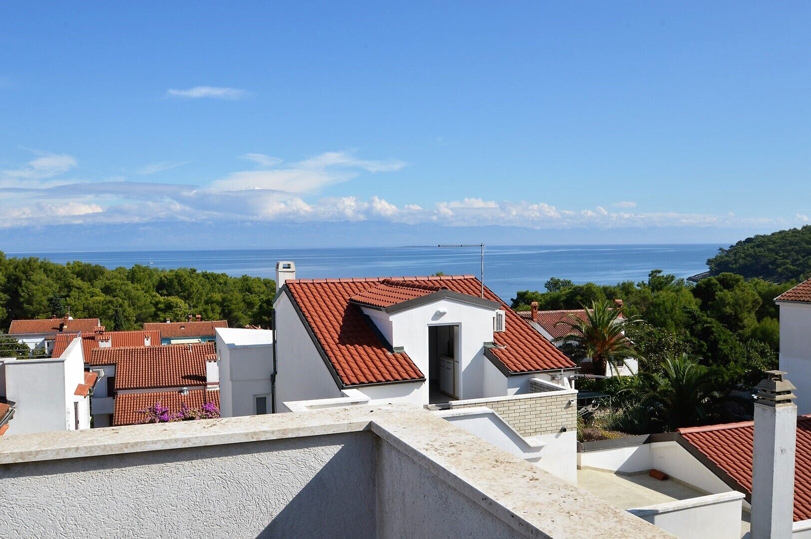 A coastal residential area with terracotta-tiled roofs, white buildings, and a view of the sea.