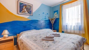 A bedroom with a bed, a nightstand, a lamp, a painting, and a window with curtains. - Two-room apartment Simpatico located in the village of Artatore. (Cunski)