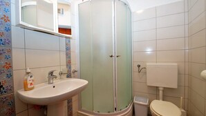 Une salle de bain avec un lavabo blanc, une douche à parois de verre, des toilettes et un miroir au-dessus du lavabo.
