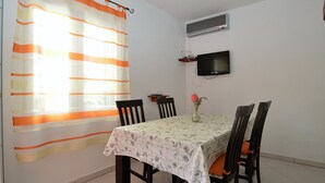 Un coin repas avec une table dressée pour quatre personnes, un téléviseur fixé au mur et un appareil de climatisation installé au-dessus.