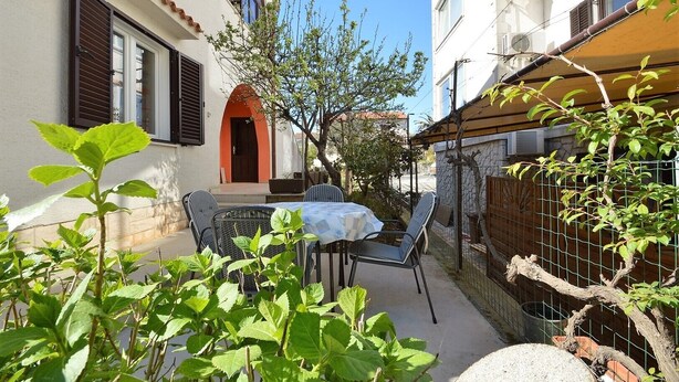 Une terrasse extérieure avec une table et des chaises, entourée de verdure et d’une clôture.