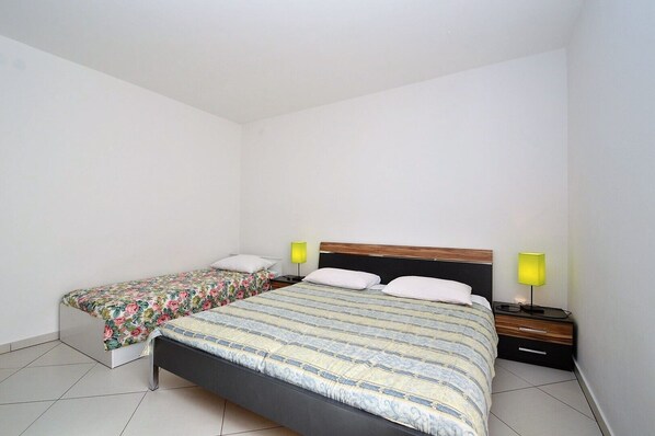 Un dormitorio con una cama grande, una cama más pequeña, dos mesitas de noche con lámparas y suelo de baldosas.