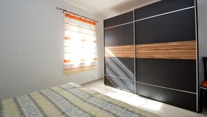 Une chambre à coucher avec un lit, une fenêtre avec des rideaux et une armoire dont le devant est orné de panneaux en bois.