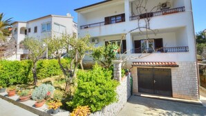 A two-story building with a balcony on the second floor, a garage, and a garden with various plants. - Studio Rahela 3 in Mali Lošinj, Zagazinjine. Suitable for 2 people. (Mali Losinj)