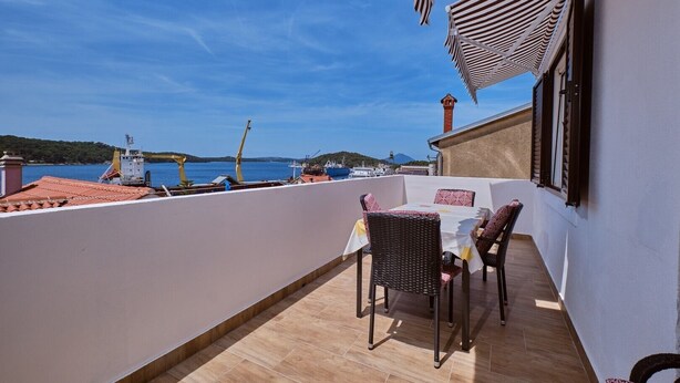 Una terraza con mesa y sillas, con vista a un puerto con barcos y grúas.