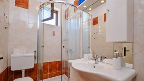 Un baño moderno con ducha de vidrio, lavamanos blanco con espejo y retrete.