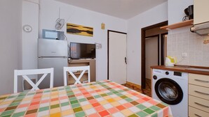Una cocina compacta con lavadora, microondas y zona de comedor con mantel a cuadros.