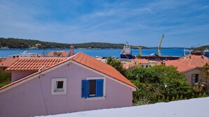 Un pueblo costero con edificios de tejados terracota, un cielo azul despejado y un gran carguero amarrado en el puerto.