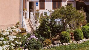 A two-story building with a balcony, a door with a sign, and a garden with various plants.