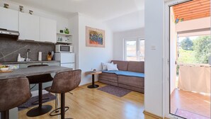 A modern kitchen with white cabinets, a dining area with a table and chairs, a sofa, and a painting on the wall.
