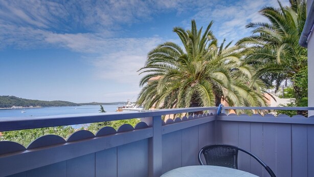 Uma varanda com vista para o mar, uma mesa com cinzeiro azul e uma cadeira.