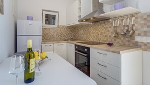 Cozinha moderna com armários brancos, forno embutido, micro-ondas e uma garrafa de vinho no balcão.