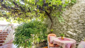 Ein Sitzbereich im Freien mit Tisch und Stühlen, einer Steinsäule und einem mit Wein bewachsenen Pergola.