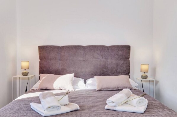 A neatly made bed with a large headboard, two bedside tables with lamps, and towels on the bed. - Apartment Blaz 1, in Mali Lošinj in a quiet location. (Mali Lošinj)