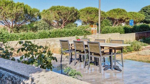An outdoor patio with a table and chairs, surrounded by greenery and trees. - Apartment Blaz 1, in Mali Lošinj in a quiet location. (Mali Lošinj)