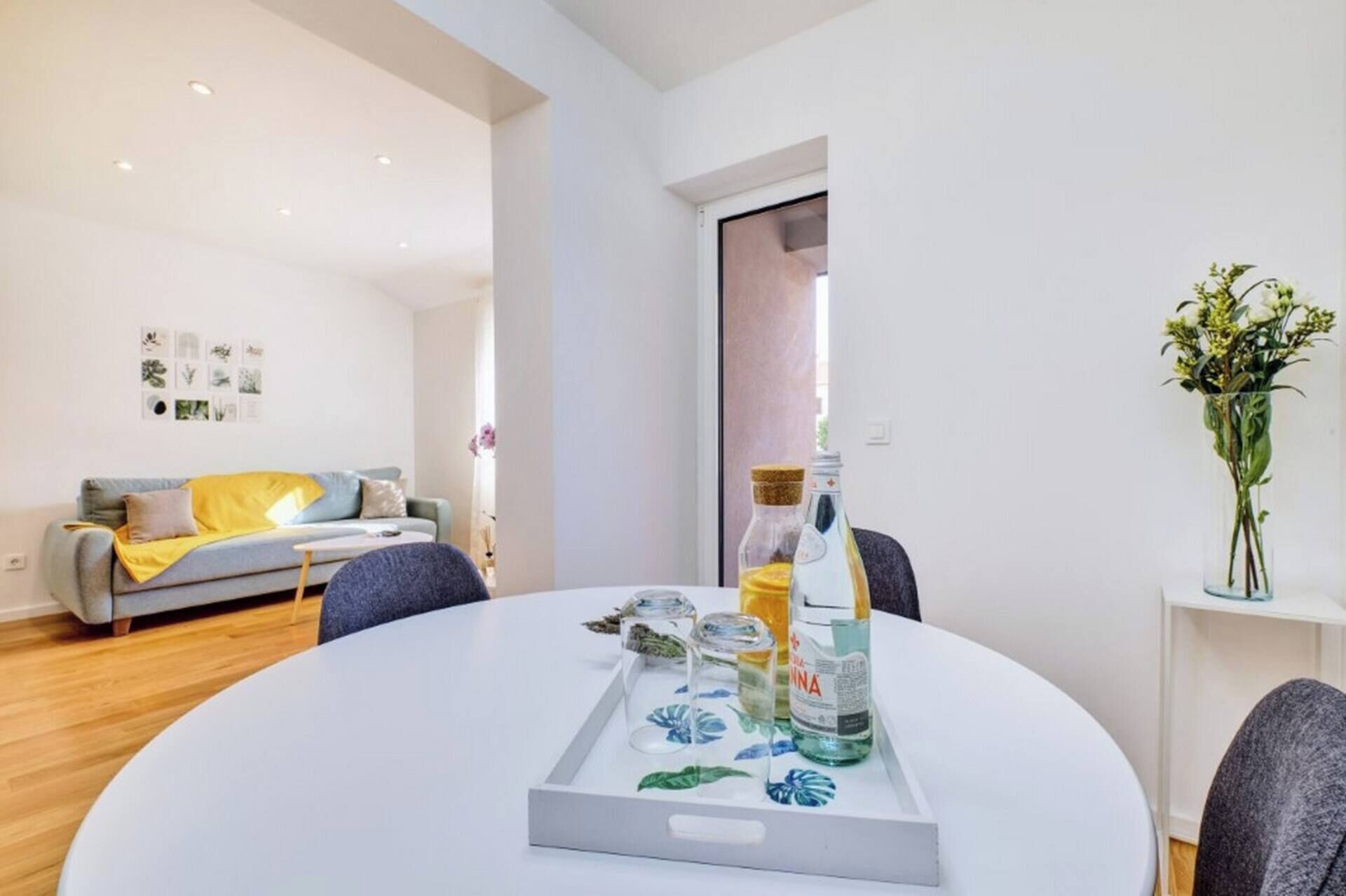Una sala de estar moderna con una mesa redonda blanca, un sofá gris y un florero con flores.
