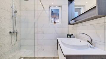 A modern bathroom with a glass-enclosed shower, a white sink, and a small window.