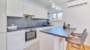 A modern kitchen with white cabinets, a grey countertop, a built-in oven, and pendant lights. - Apartment Blaz 1, in Mali Lošinj in a quiet location. (Mali Lošinj)