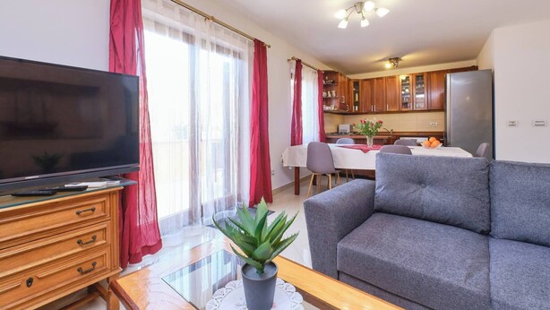 A living room with a flat-screen TV, a grey sofa, a wooden coffee table, and a dining area with a table and chairs. - Apartment Dino 1, situated on the ground floor, ideal for four people. (Mali Lošinj)