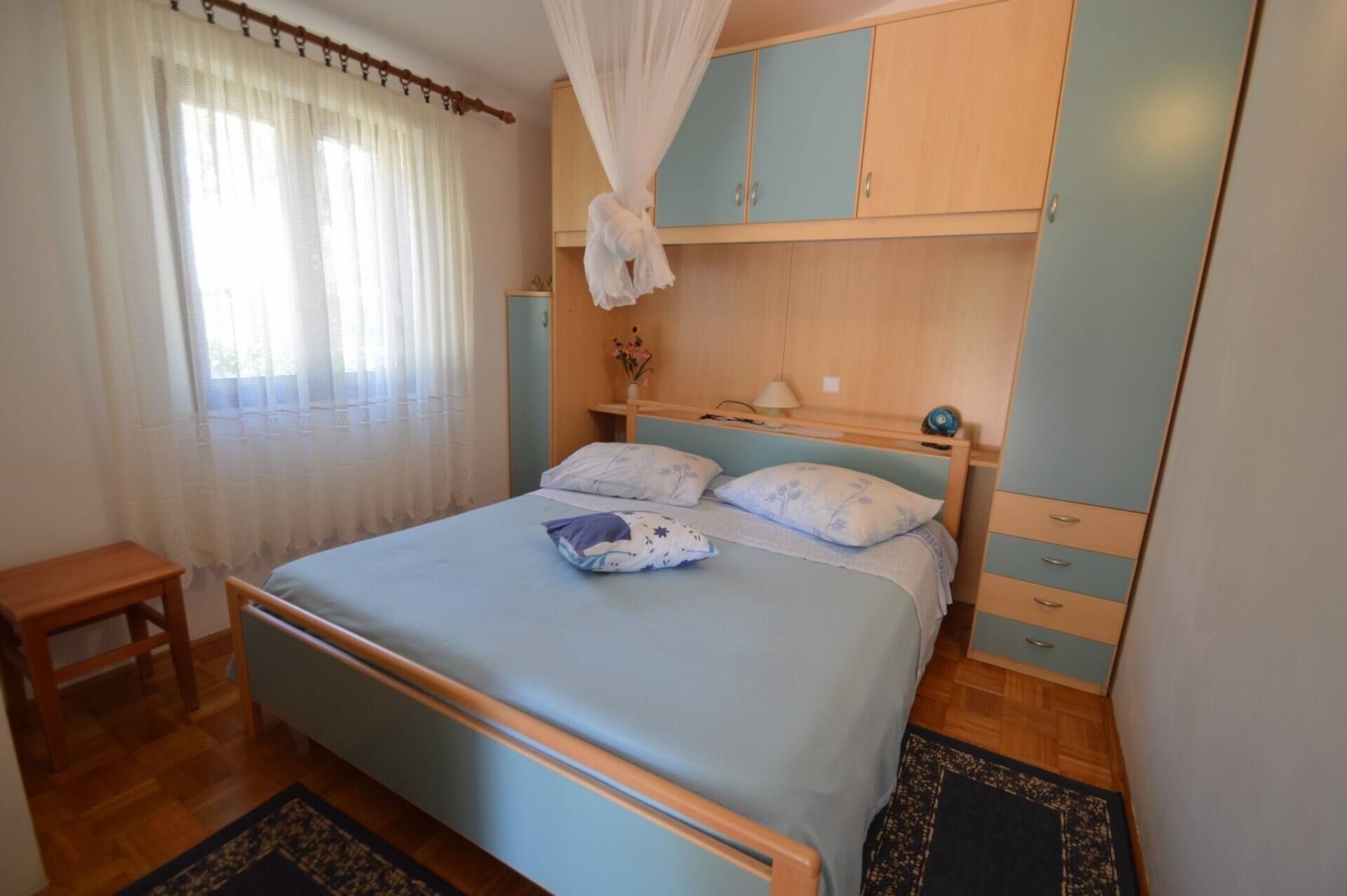 Une chambre à coucher avec un lit, une table de chevet, une armoire et une fenêtre avec des rideaux.