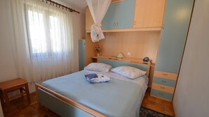 Un dormitorio con cama, mesita de noche, armario y ventana con cortinas.