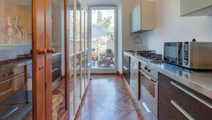 Cocina estrecha con suelo de madera, estufa a gas, microondas y vistas a un patio exterior.