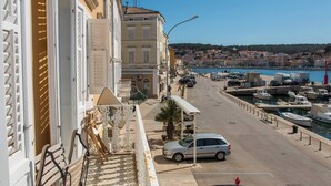 Una calle costera con un puerto deportivo, edificios con balcones y una vista despejada del pueblo al otro lado del agua.