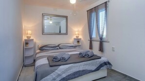 Une chambre à coucher comprenant un lit, deux lampes de chevet, un ventilateur de plafond, une fenêtre avec des rideaux et un miroir au mur.