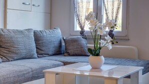 Un salon moderne avec un canapé gris, une table basse blanche et un vase rempli d’orchidées blanches.