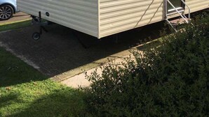 Ein Wohnmobil mit einem Schild mit der Aufschrift 'Sunrise'. Es hat eine kleine Veranda und ein Fenster mit Blick auf ein Haus.