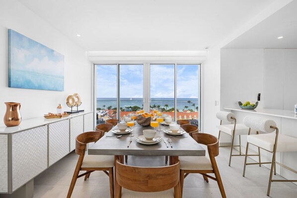 Un comedor moderno con una mesa grande dispuesta para el desayuno, con vistas a un paisaje marino.