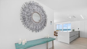 A modern kitchen with a large island, a decorative mirror, and a teal bench with candles.