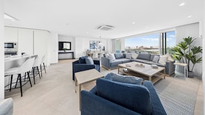 A modern living room with a sofa set, a coffee table, and a dining area with chairs and a table. - Luxury Coastal Condo with Panoramic Views of Aruba (Noord)