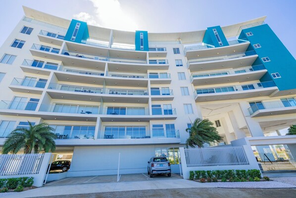 A multi-story hotel with balconies, a parking area, and a clear sky.