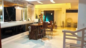 A modern dining area with a high ceiling, a dining table with chairs, and a view of the outside through large windows.