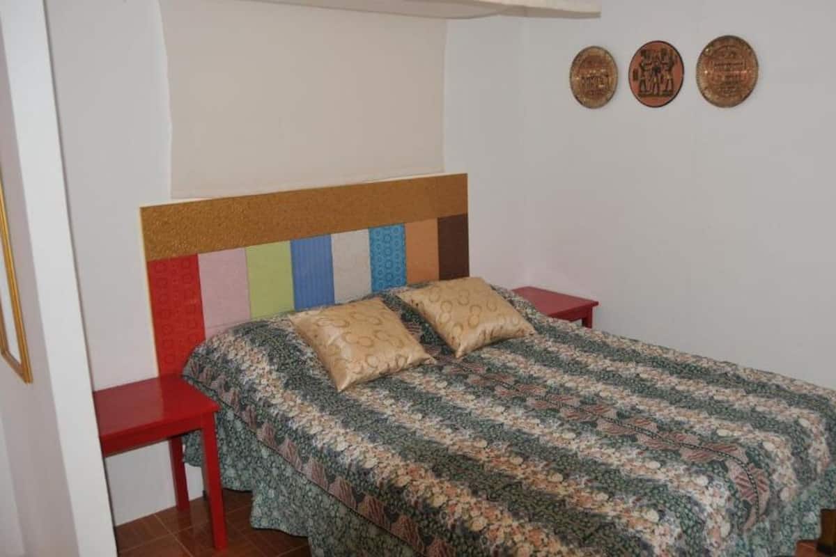 A bedroom with a bed, two nightstands, a wooden headboard, and three wall plaques.