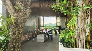 A dining area with a table and chairs, surrounded by bamboo plants and a tree.