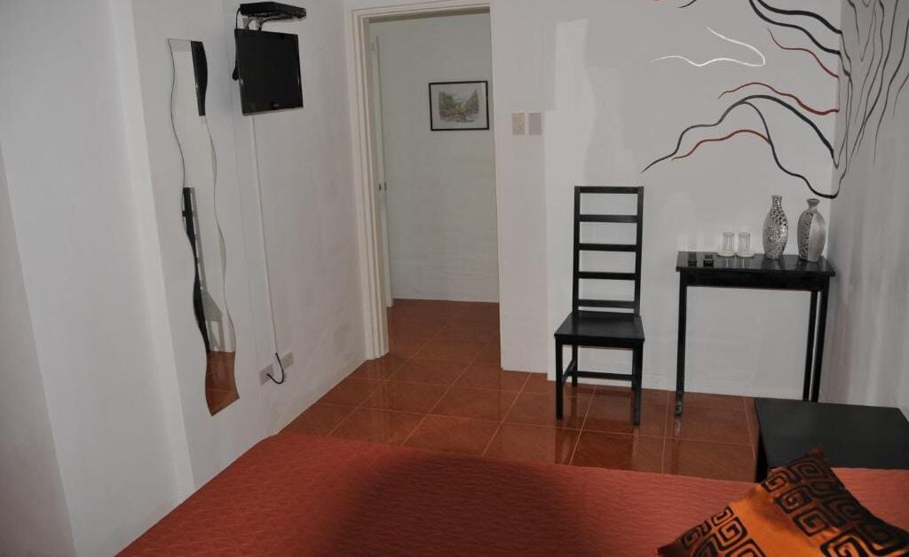 A hotel room with a bed, a desk, a chair, and a door leading to another room.