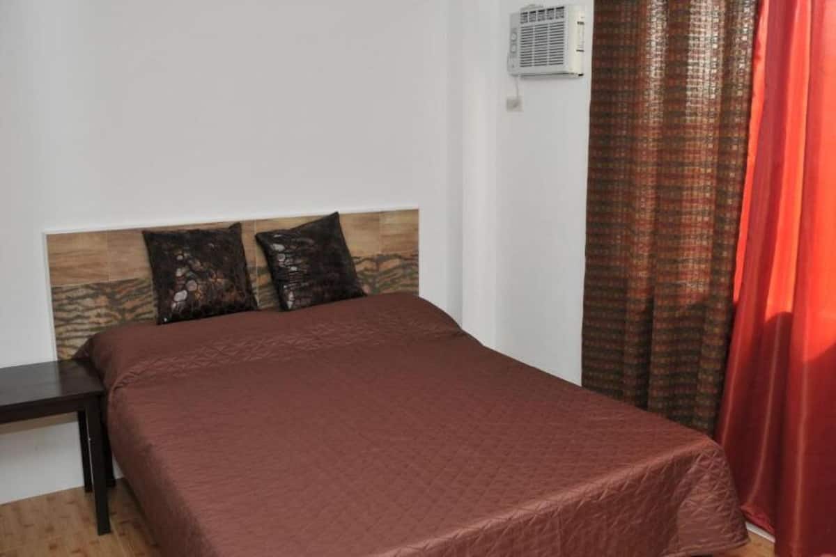A single bed with a wooden headboard, a bedside table, and a red curtain.