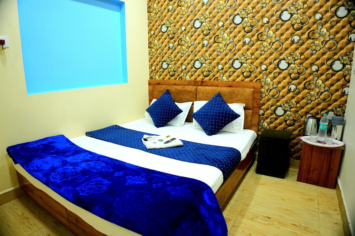 A hotel room with a bed, a wooden headboard, a patterned wall, and a small wooden side table with a water bottle and glasses.