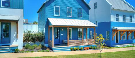 Une rangée de maisons bleues, chacune dotée d’un porche abrité et d’un petit jardin devant.